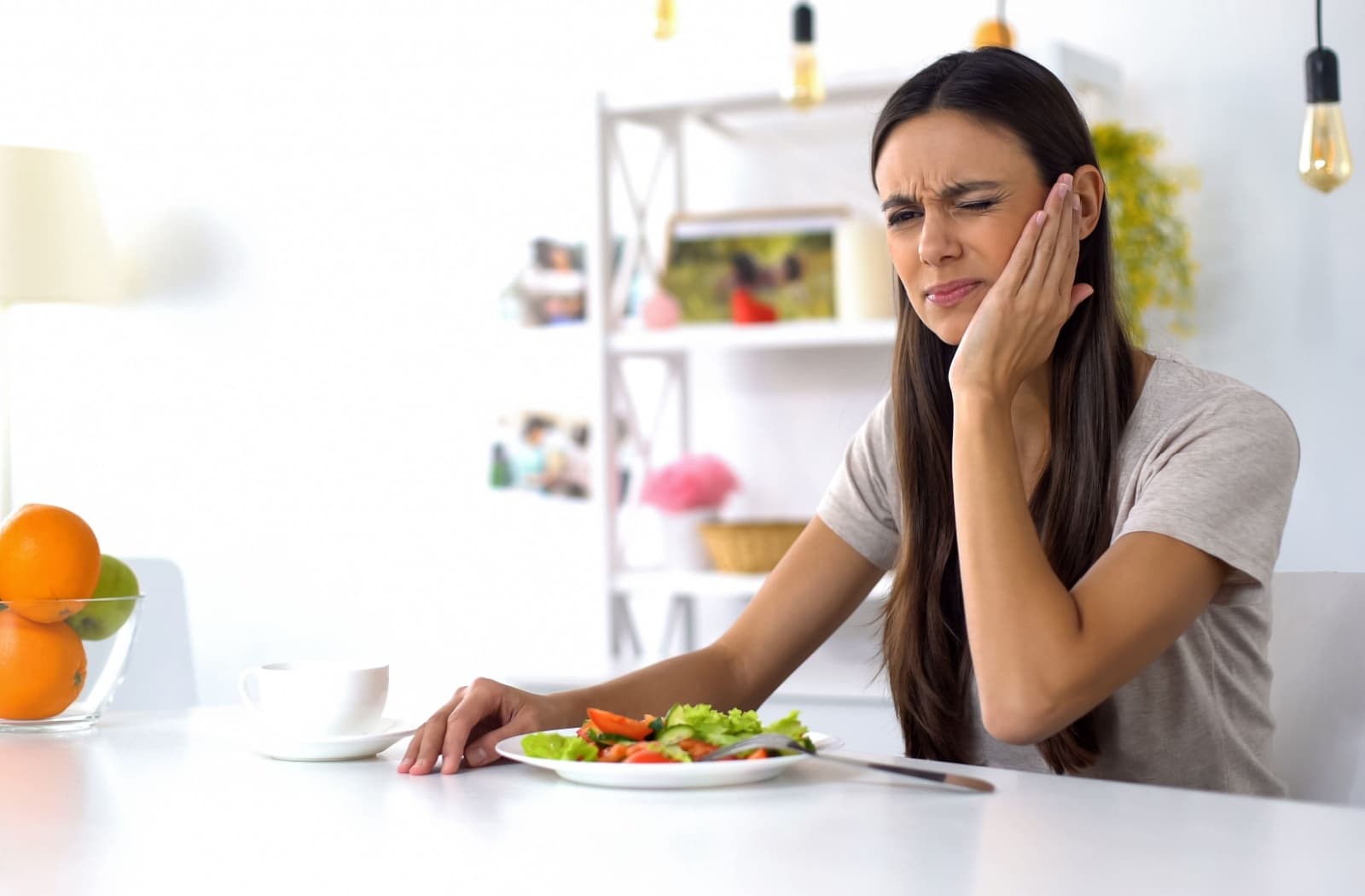 A person eating a salad holds their painful jaw.