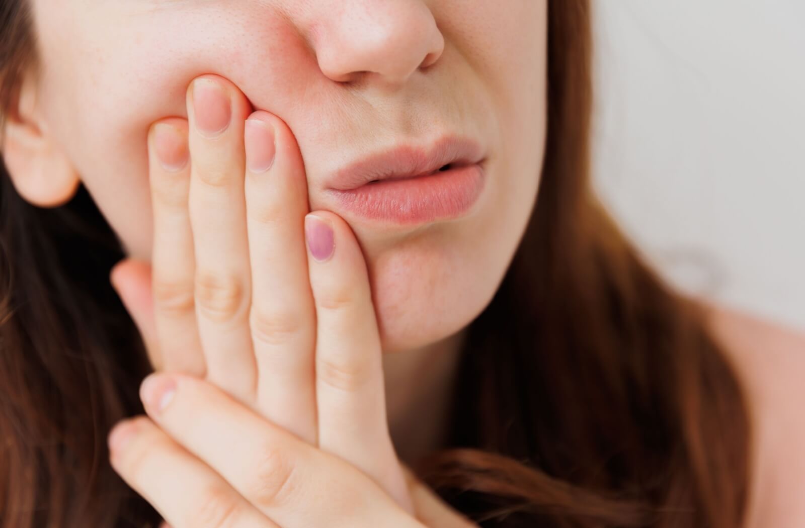 A close-up image of a person holding the side of their mouth from a pulsating toothache.