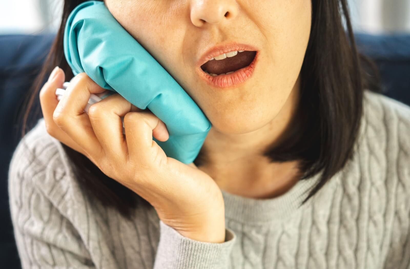 A person holds a cold compress against their right cheek to soothe a toothache.