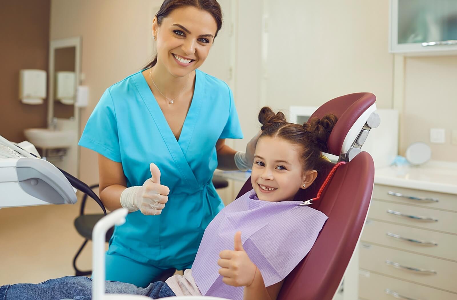 A child and dental assistant give a thumb's up to the camera