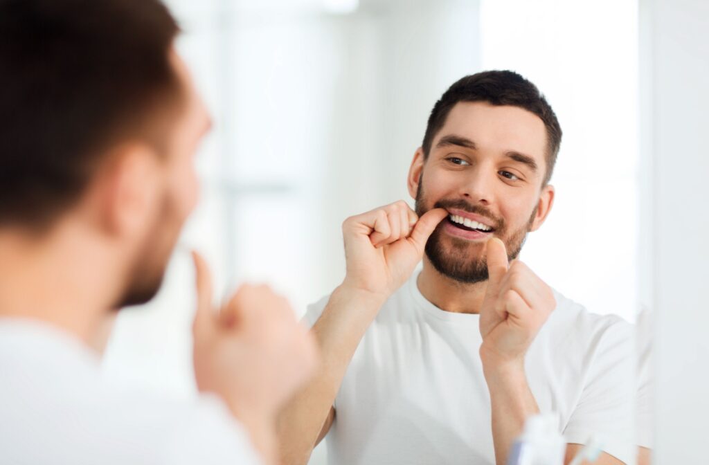 A person looking in the mirror flossing their teeth.