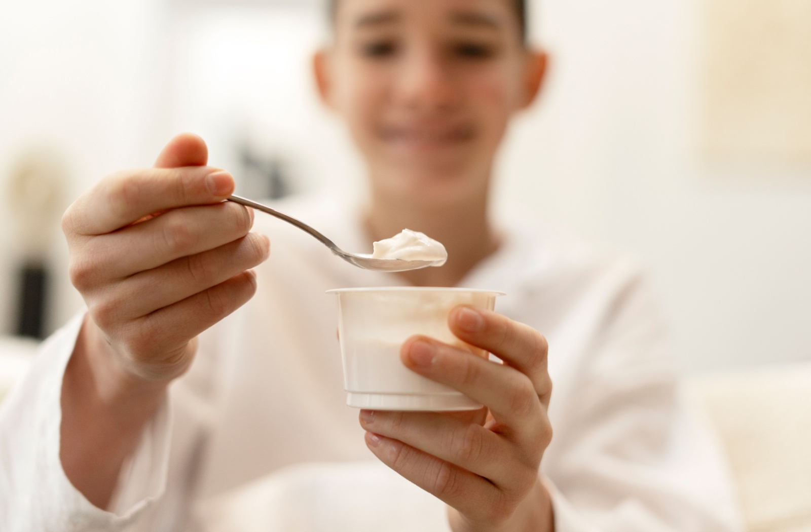 A person holding out a cup of yogurt and a spoon, showing what they're eating after wisdom tooth removal.