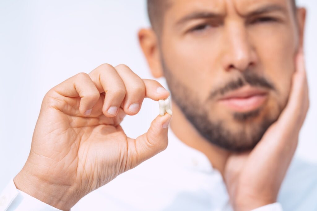A person holding their jaw in one hand and a tooth that has been removed in their other hand.