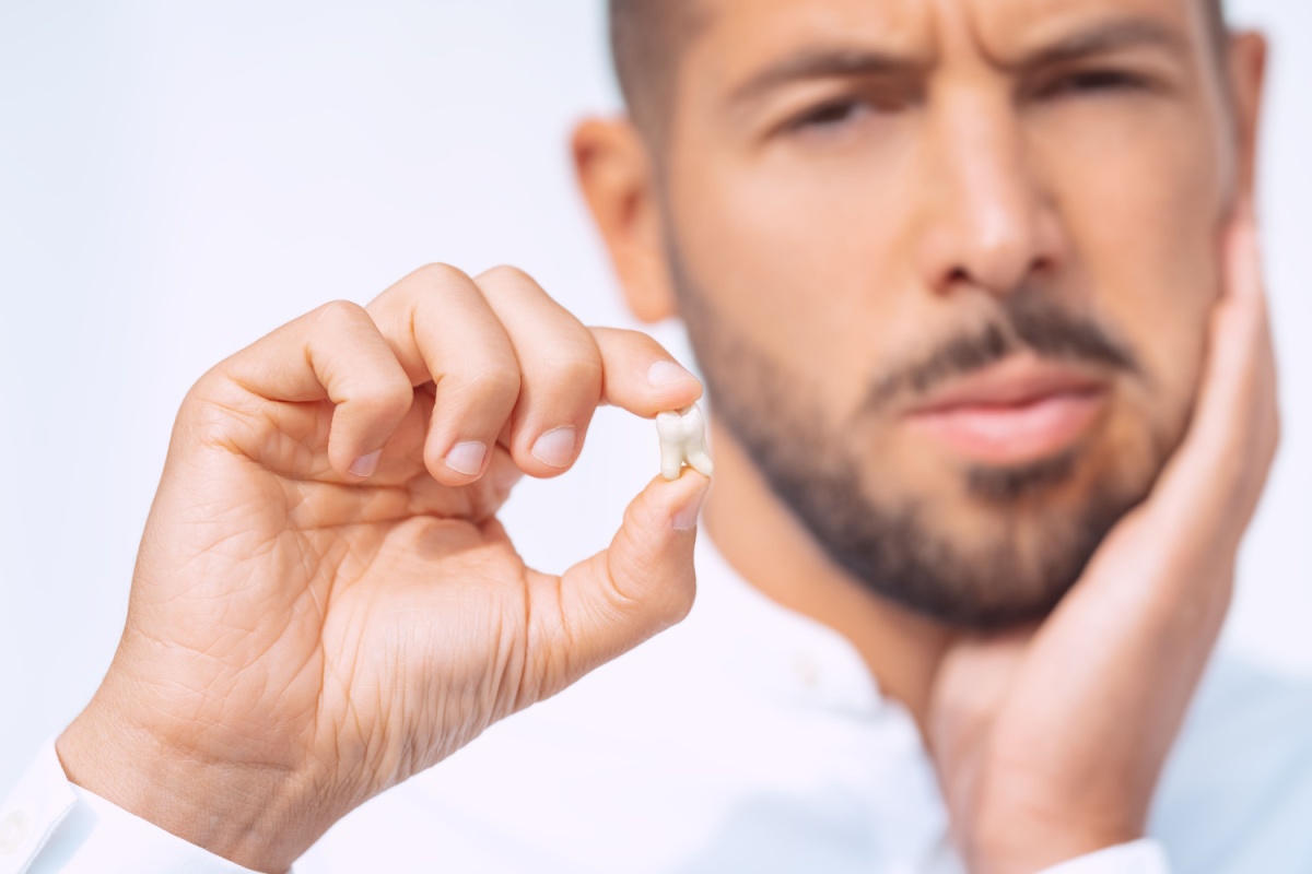 A person holding their jaw in one hand and a tooth that has been removed in their other hand.