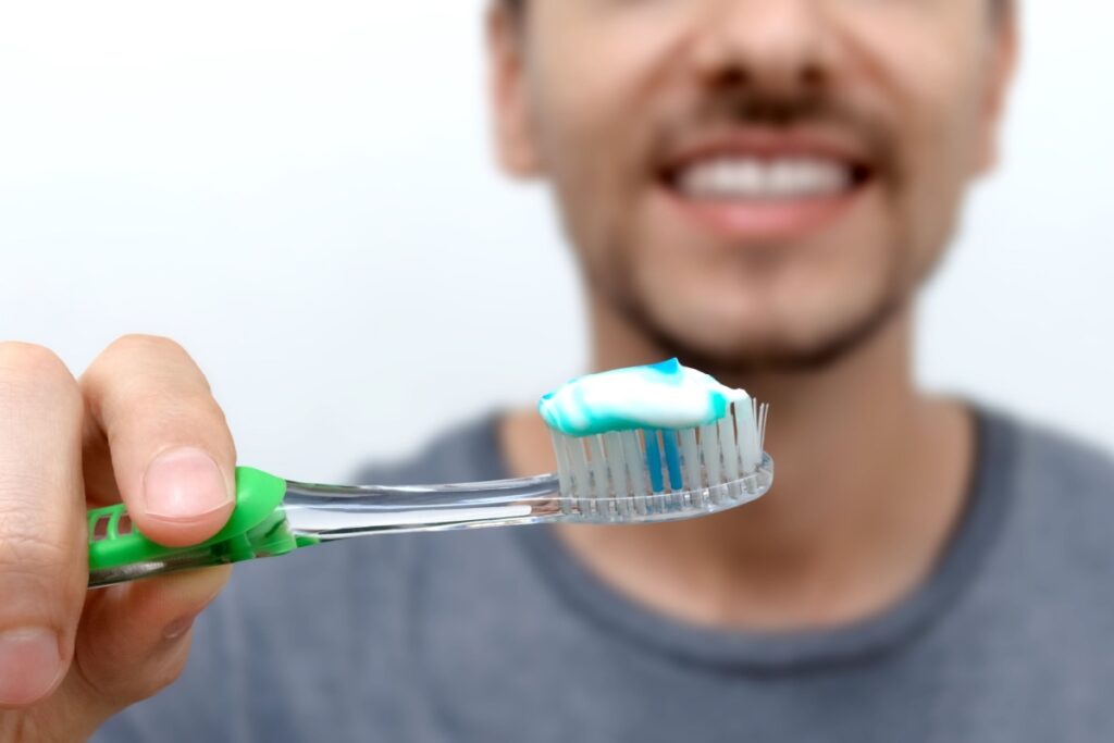 A person holding out a toothbrush with toothpaste on it.