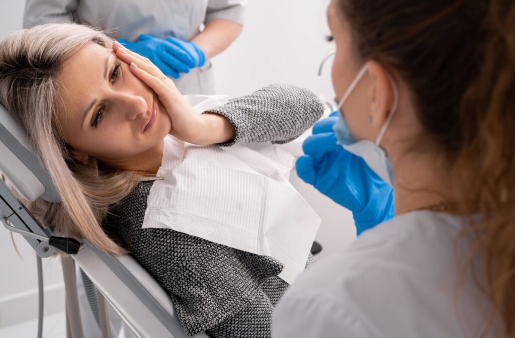 A person laying down in a dental chair and holding their jaw due to discomfort caused by a dental emergency